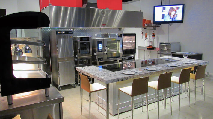 Demo commercial kitchen with wooden chairs/high chairs, stainless steel tables, kitchen counter and stainless steel commercial appliances